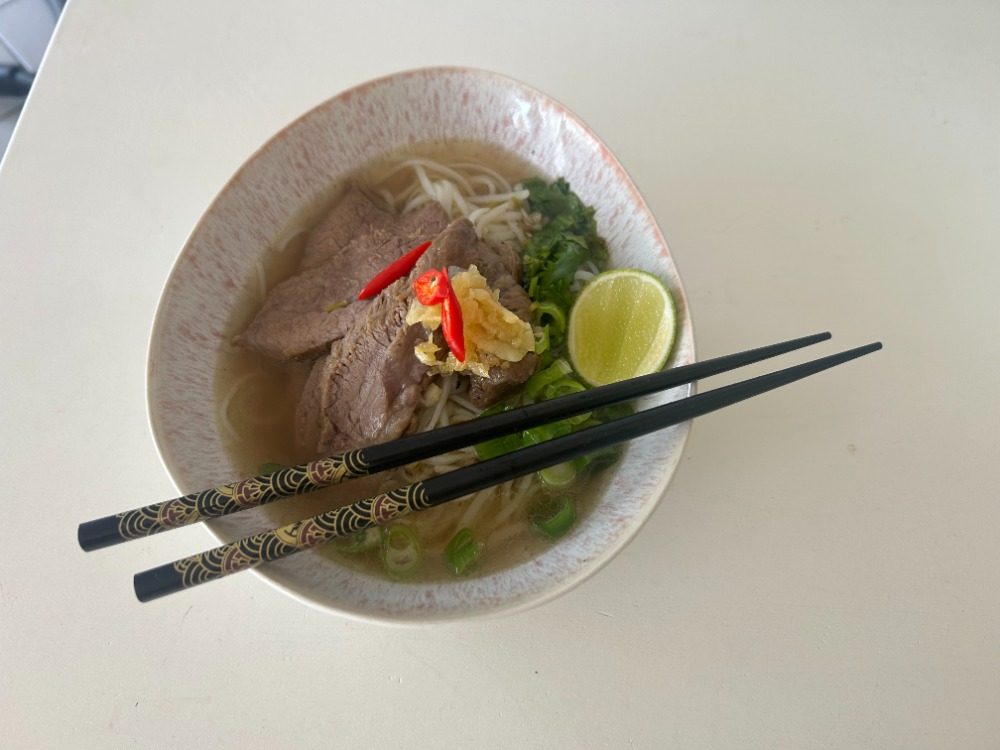 Nudelsuppe mit Rindfleisch, Limette und Frühlingszwiebeln, Stäbchen liegen auf der Schale